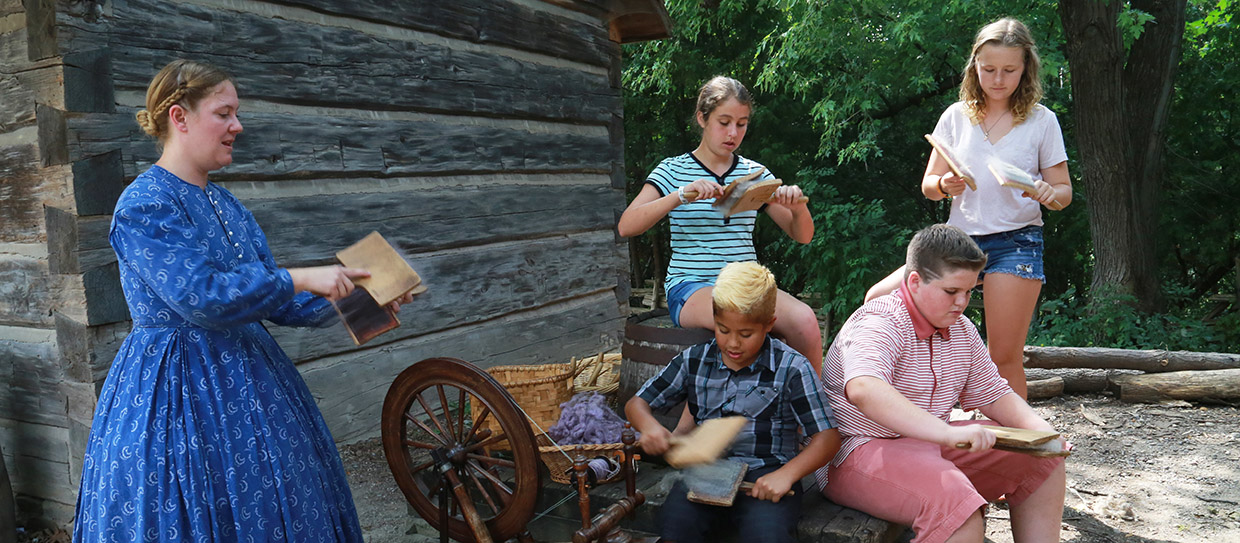 Black Creek heritage interpreter in period costume demonstrates carding wool for students