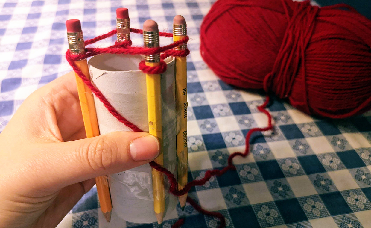 crafter wraps yarn around outside of pegs