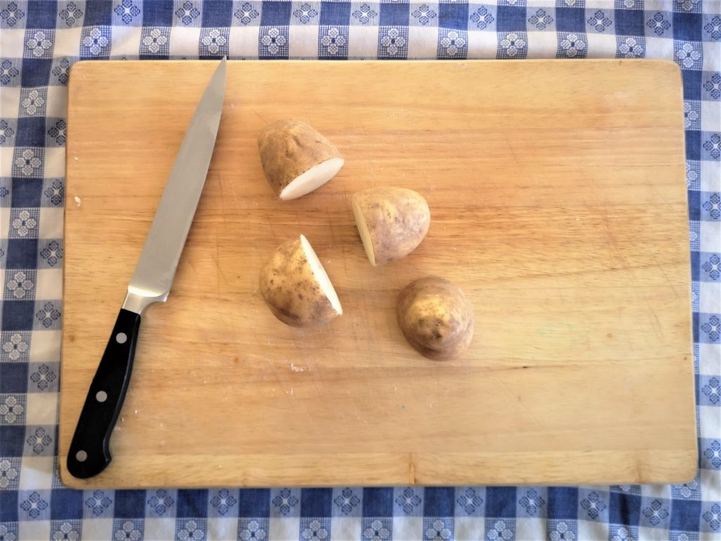 Four halves of a potato on a cutting board with a kitchen knife