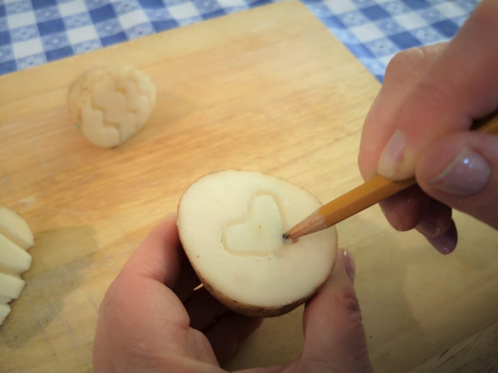 A hand drawing a heart into half of a potato