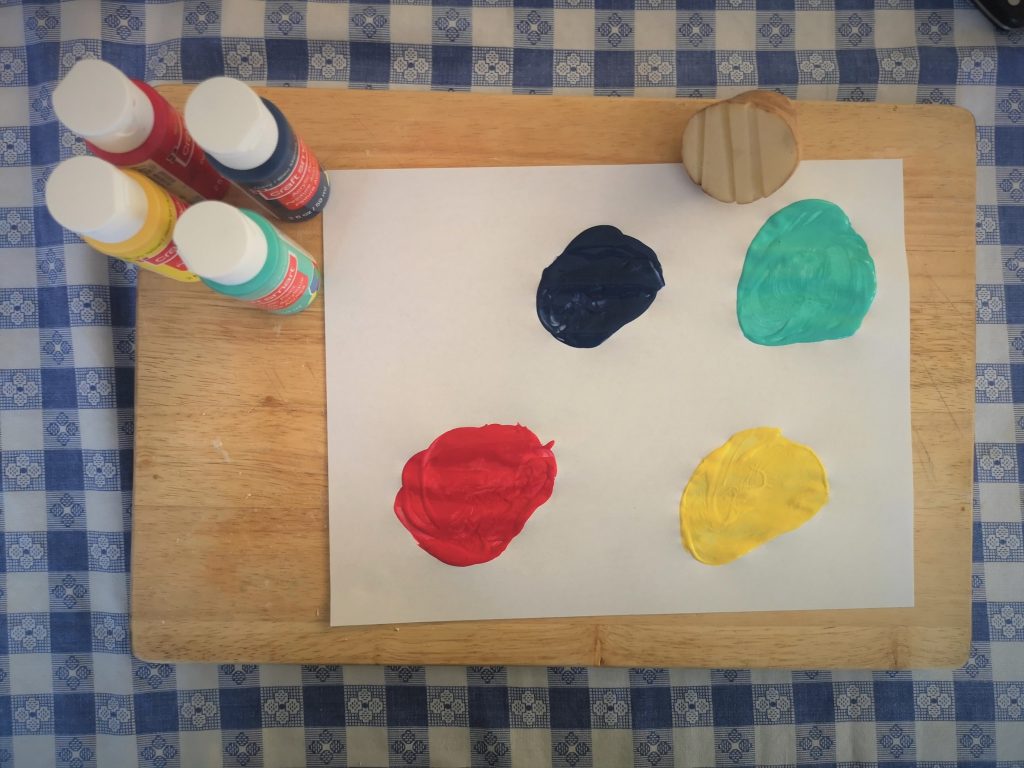 A sheet of paper with four circles of paint next to four bottles of paint