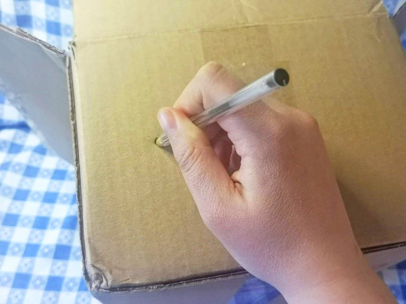 crafter uses pen to punch pinhole in cardboard box to make camera obscura
