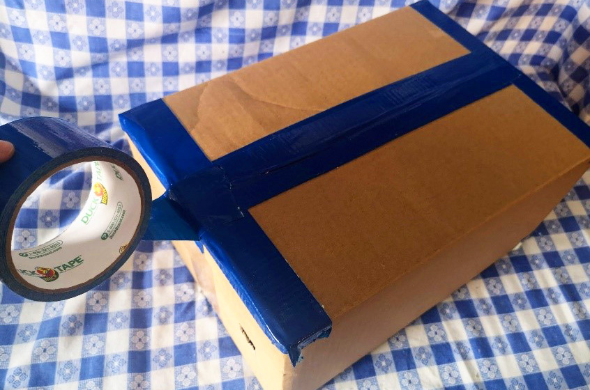 crafter uses heavy-duty tape to seal cardboard box and prevent light from leaking into camera obscura