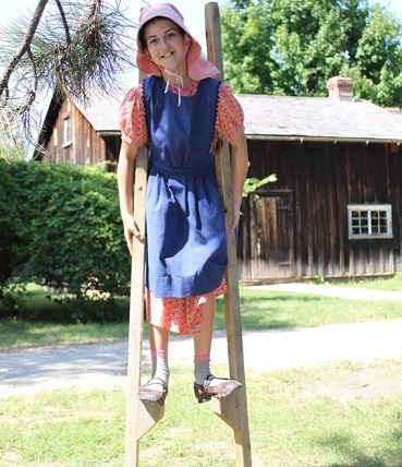 girl in 19th century costume practices walking on stilts at Black Creek Pioneer Village