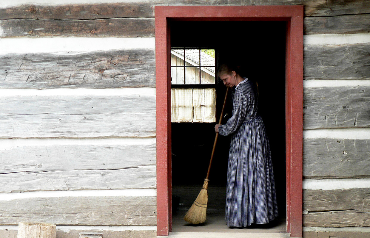 history actor with broom sweeps doorway of first Daniel Stong house at Black Creek Pioneer Village