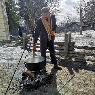 costumed educator at Black Creek Pioneer Village brings kettle to boil over fire to make maple syrup