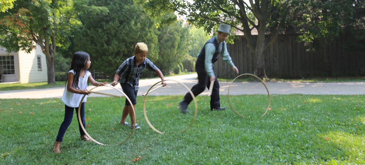 costumed educator and students play Victorian-style rolling hoop game at Black Creek Pioneer Village