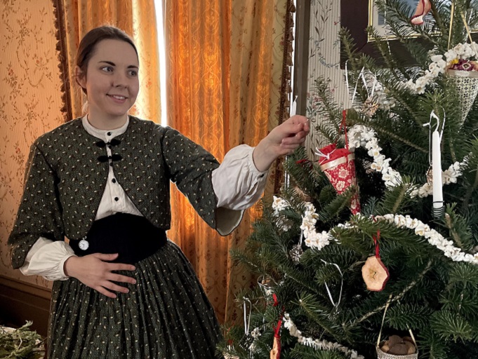 historical educator in Victorian costume trims Christmas tree with traditional ornaments