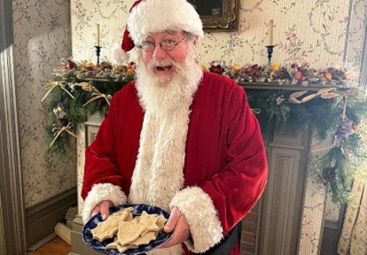 Santa Claus offers plate of cookies to holiday visitors at Black Creek Village