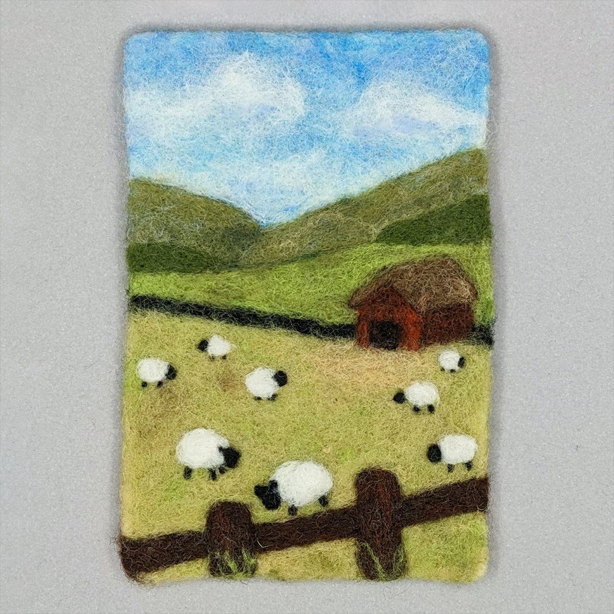a needled felted wool painting of a summer landscape with sheep