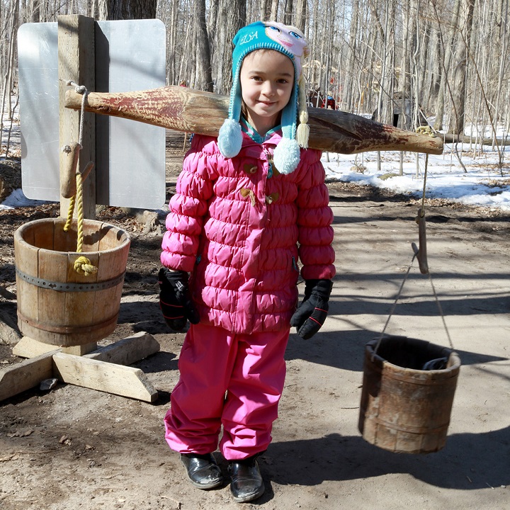 girl practices using a yoke to carry sap buckets during Maple Days at the Village event at Black Creek Pioneer Village