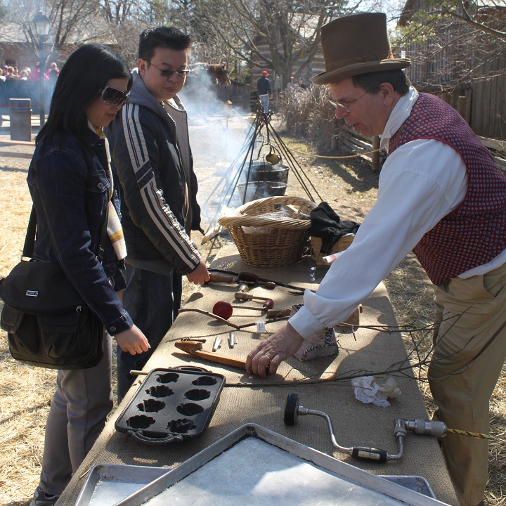 costumed educator at Black Creek Pioneer Village demonstrates traditional 19th century implements used for collecting sap and making maple syrup