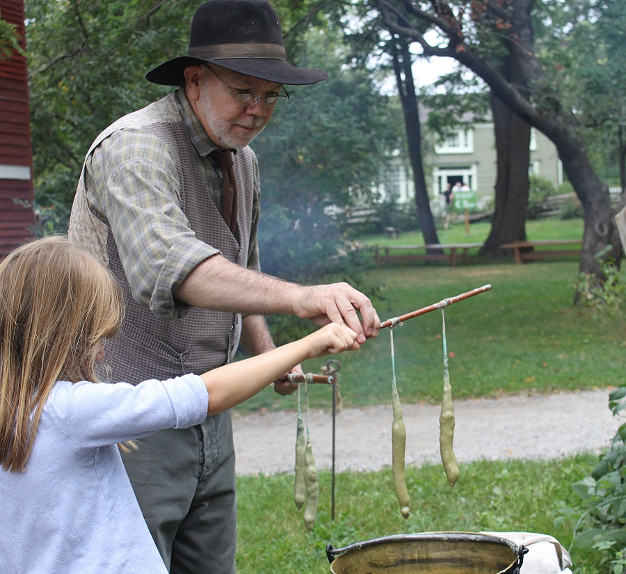 costumed educator at Black Creek Pioneer Village Fall Festival demonstrates the traditional 19th century method of candle dipping