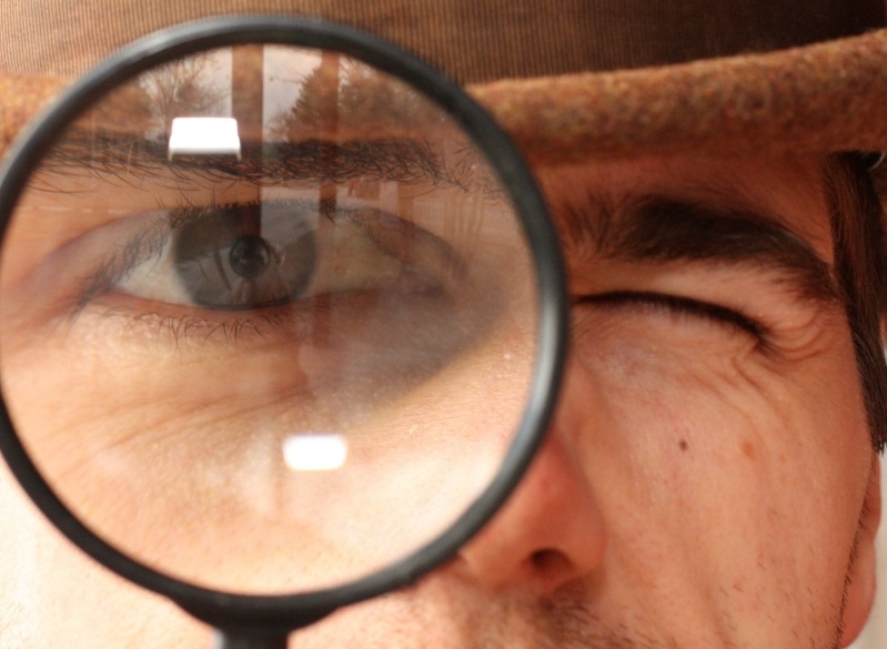 old-fashioned Victorian detective in the style of Sherlock Holmes peers through a magnifying glass in search of clues