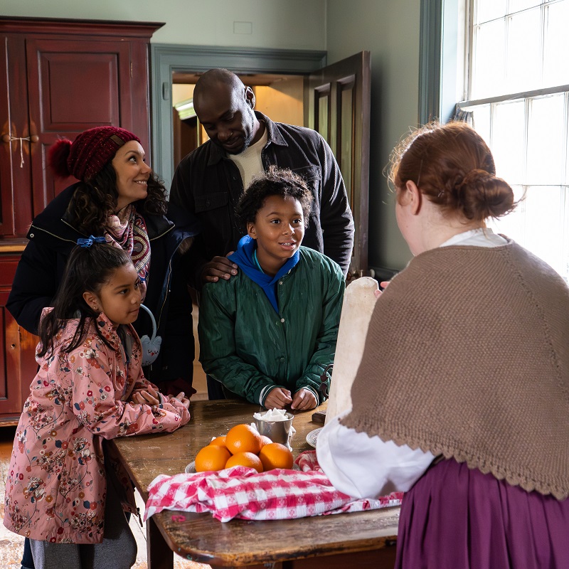 a young family encounters a costumed educator inside one of the heritage buildings at Black Creek Pioneer Village