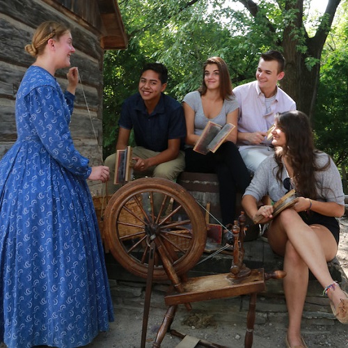 Costumed educator at Black Creek Pioneer Village shows students how to use a 19th century spinning wheel