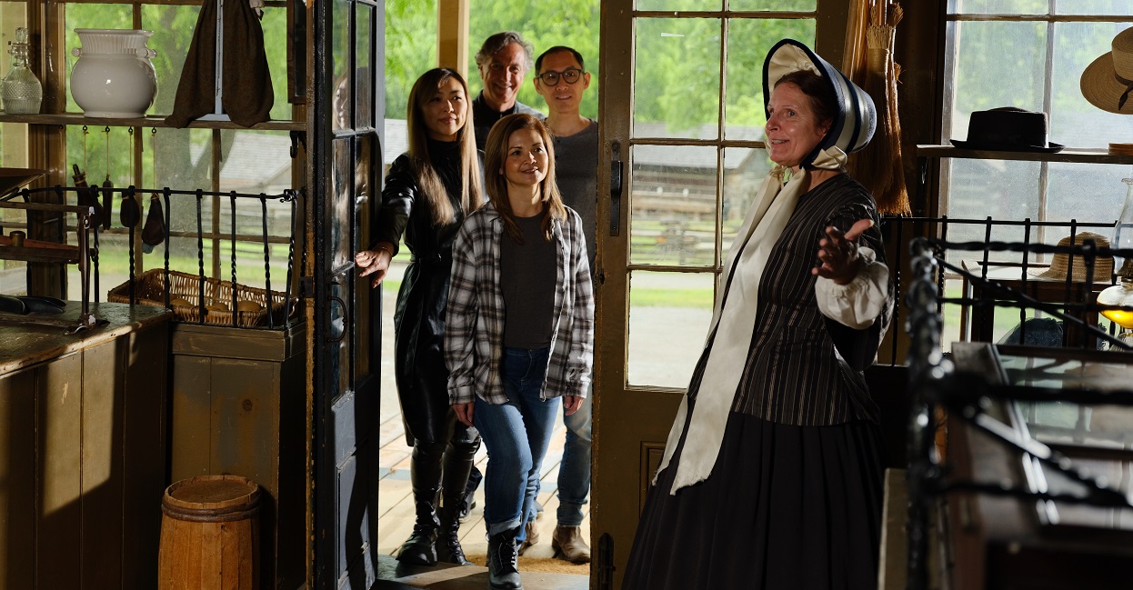 a costumed historian leads a family on a guided tour of a heritage building at the Village at Black Creek