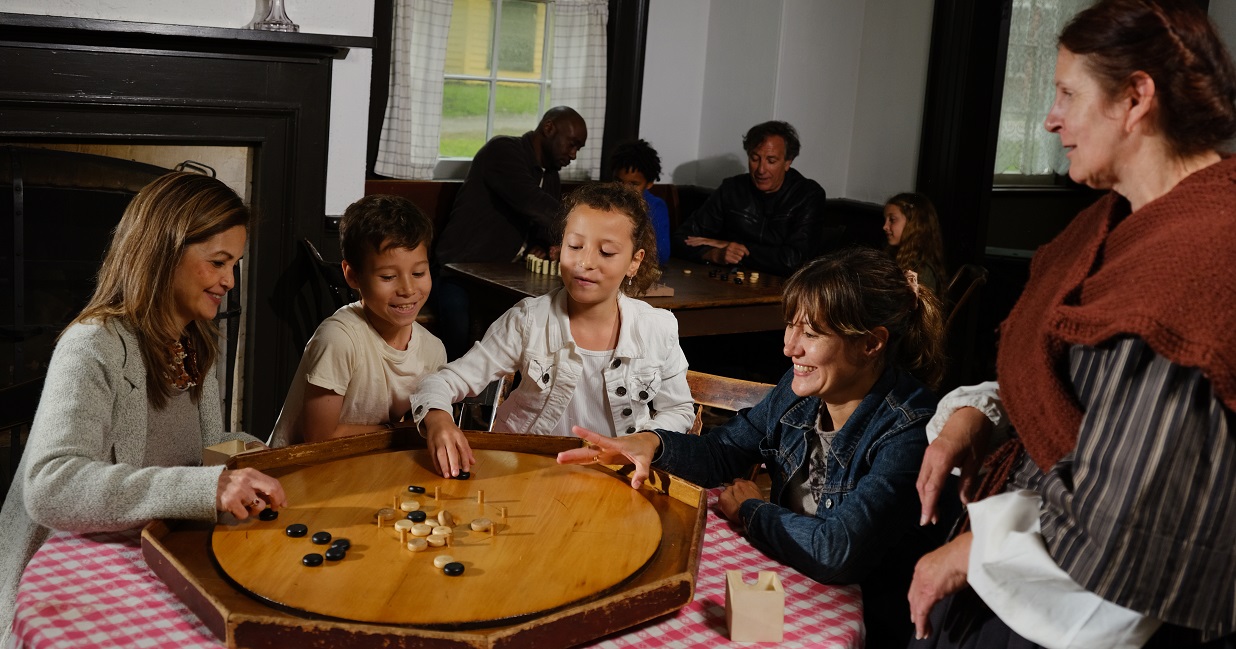 a young family learns to play a 19th century board game during a self-guided weekend visit to the Village