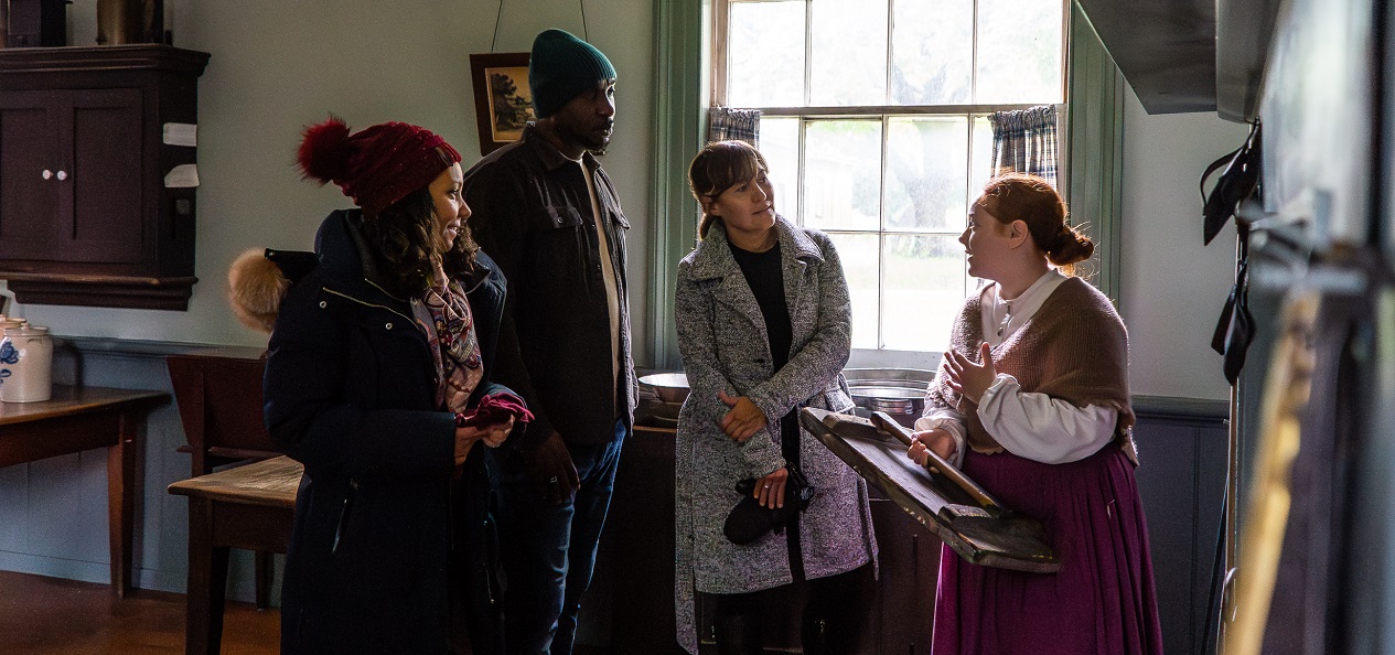 a costumed historian guides visitors through a heritage building at the Village at Black Creek