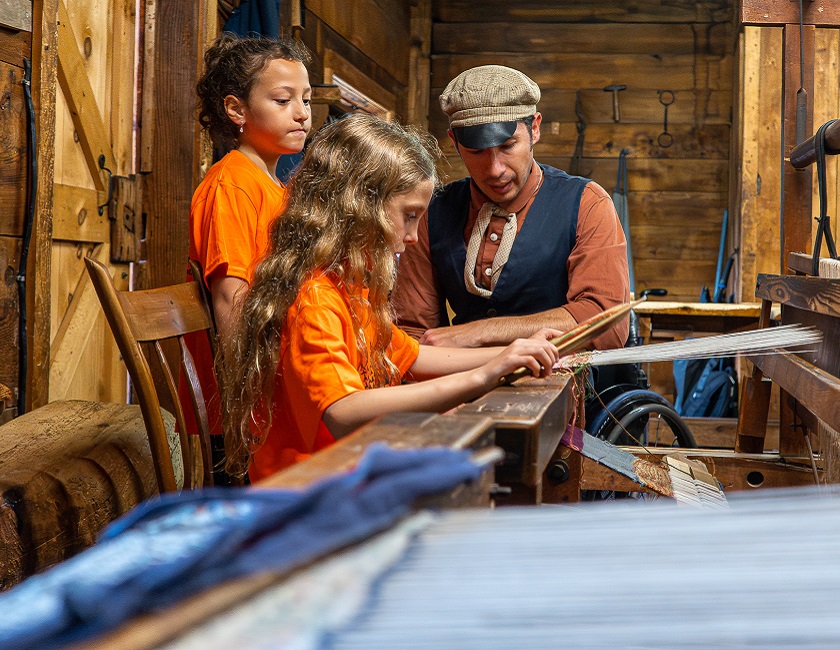 a costumed educator at the Village at Black Creek teaches young visitors how to use a traditional 19th century loom