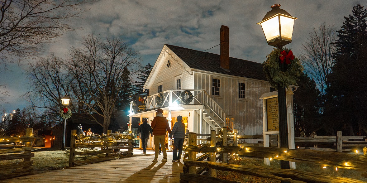 visitors explore The Village at Black Creek by lamplight during the Festive Nights holiday celebration