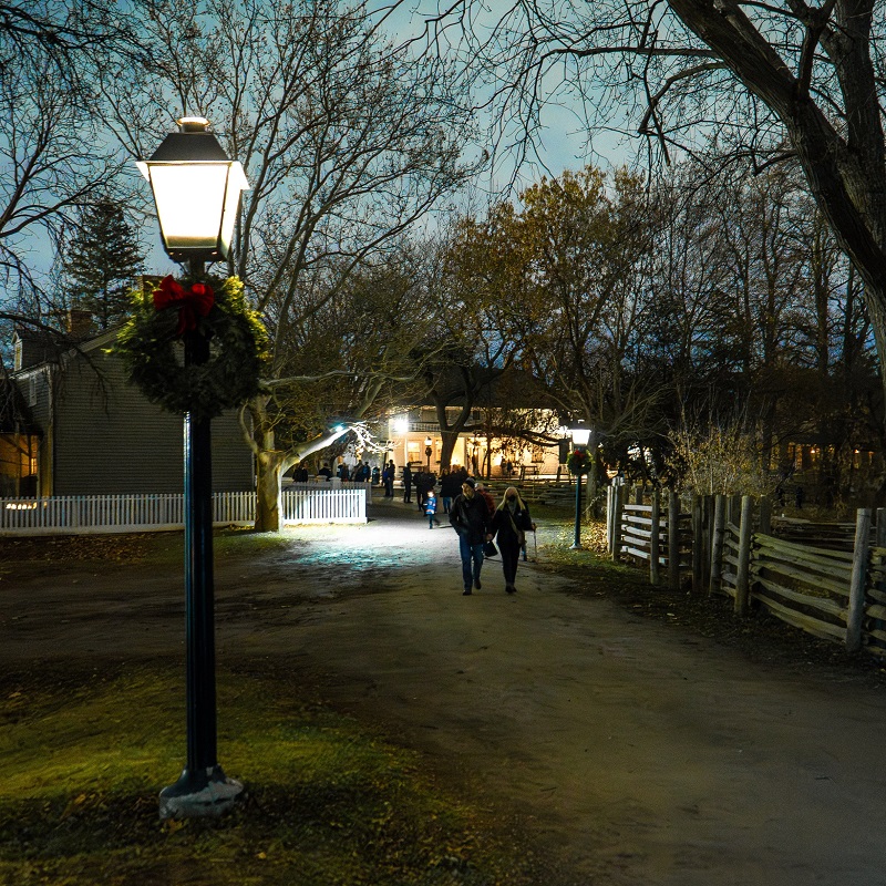 visitors explore The Village at Black Creek by lamplight during the Festive Nights holiday celebration