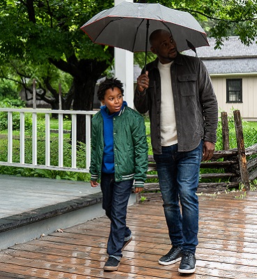 a father and son explore The Village at Black Creek under an umbrella on a rainy day