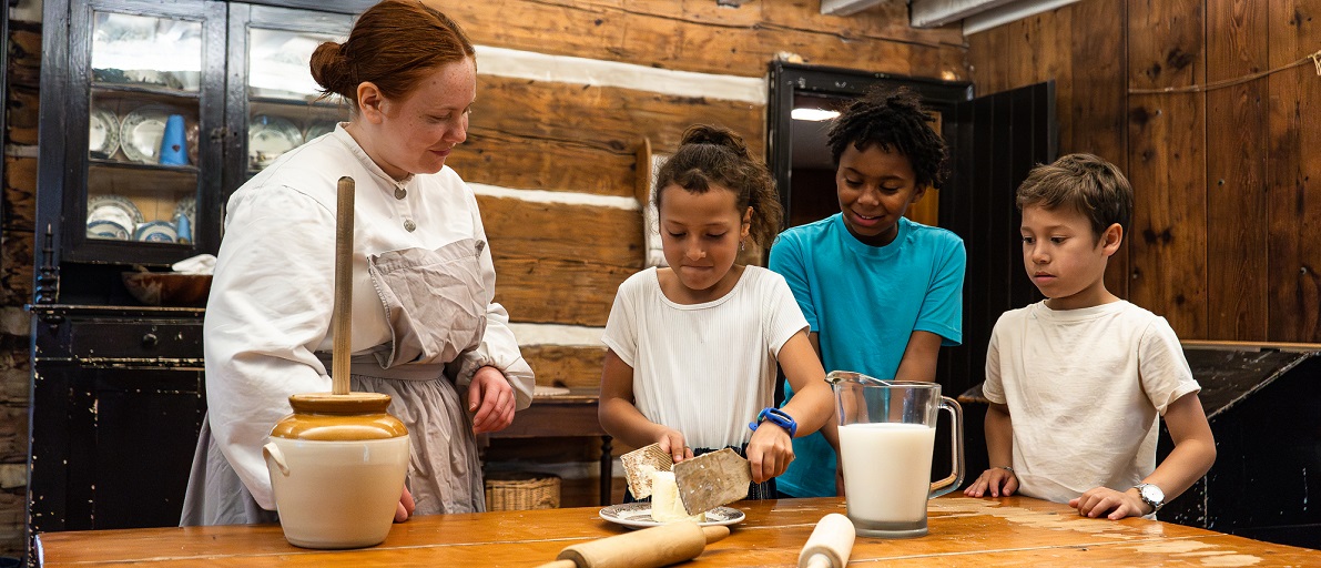 a costumed educator teaches summer campers at The Village at Black Creek how to make butter