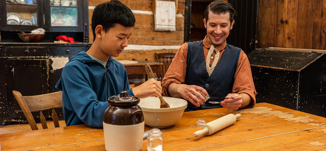 a costumed educator at The Village at Black Creek teaches a summer camper the techniques of 19th century cooking