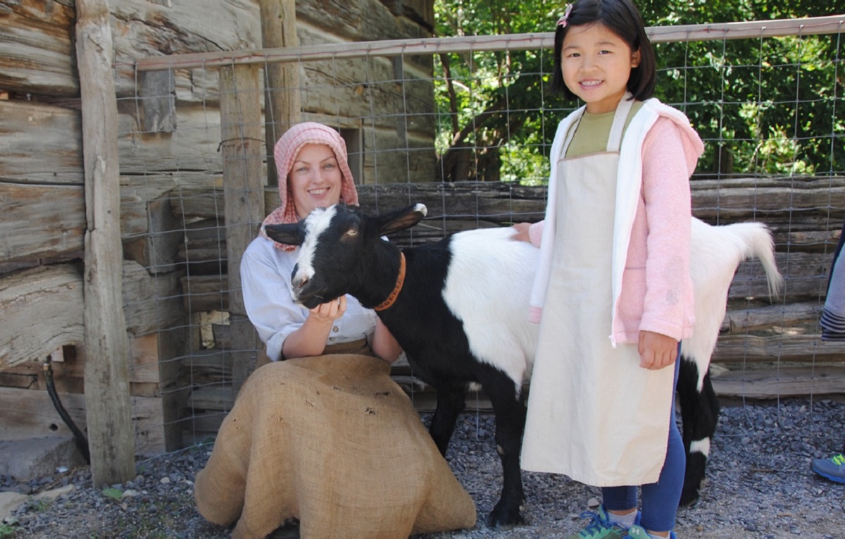Summer Camp & Teen Experiences at The Village 14 a costumed educator introduces a summer camper to a goat at The Village at Black Creek