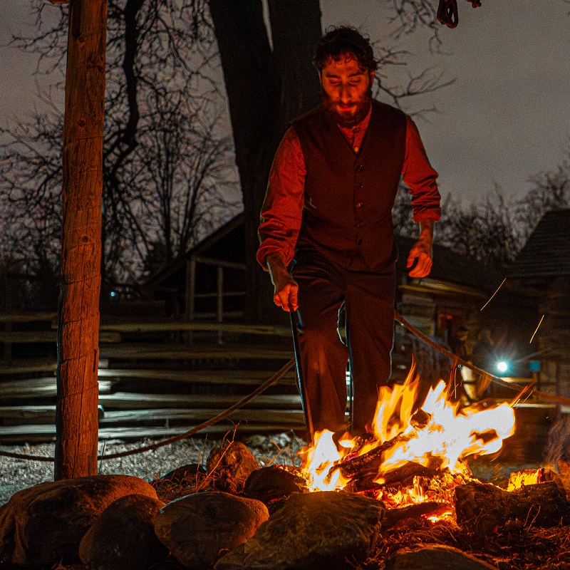 a costumed educator tends to a fire at the Festive Nights event at The Village at Black Creek