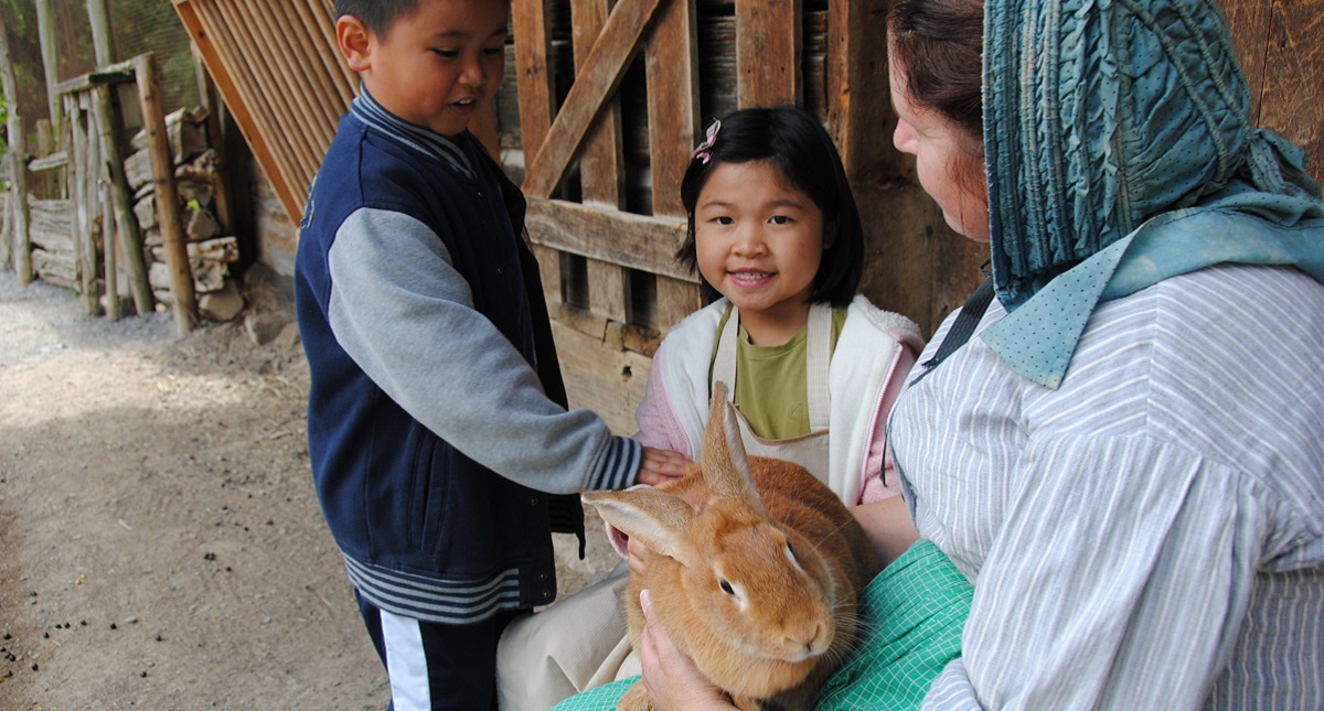 a costumed educator at The Village at Black Creek introduces two young visitors to a rabbit