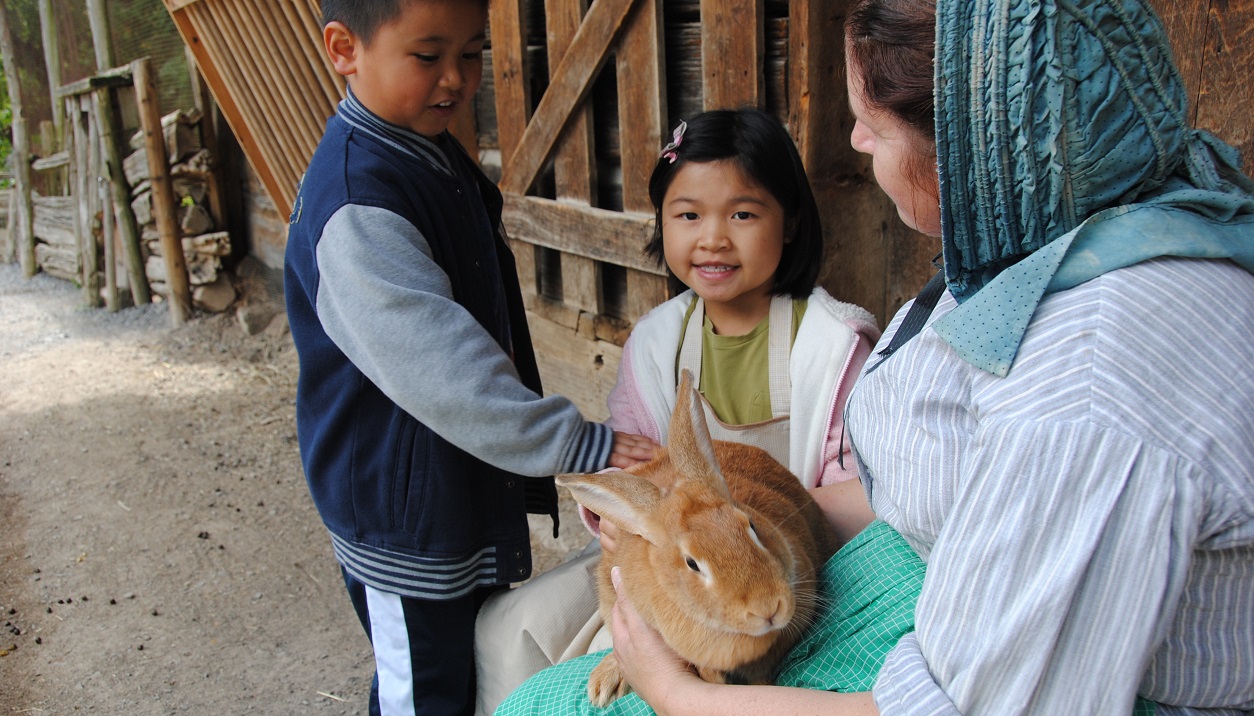 a costumed educator at The Village at Black Creek introduces two young visitors to a rabbit