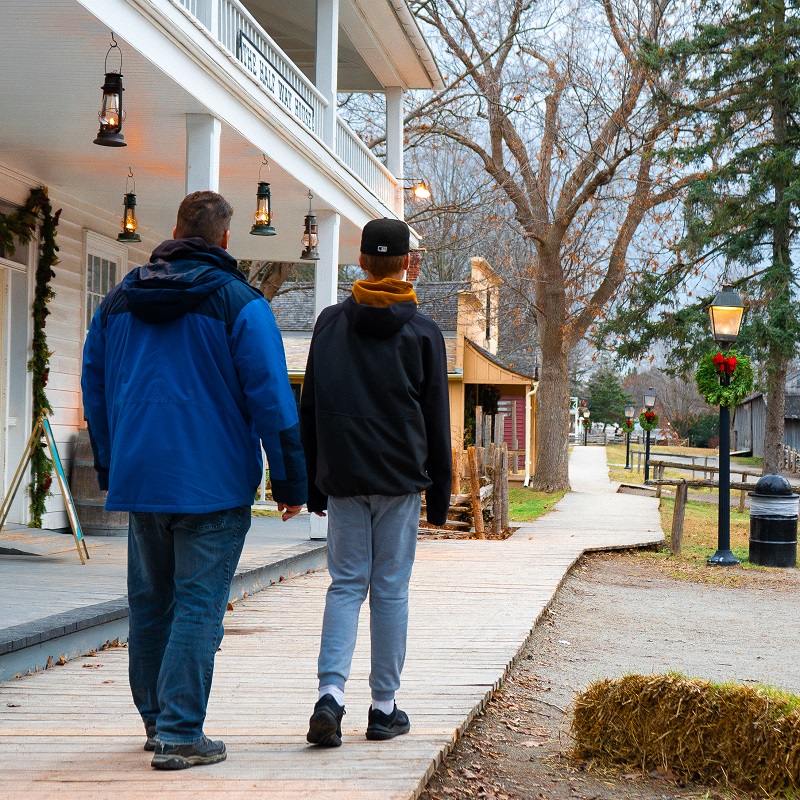 a father and son explore a street lined with holiday decorations at The Village at Black Creek