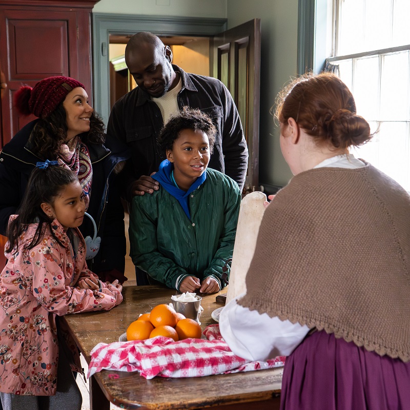 Holidays at The Village 13 a costumed educator in a heritage building welcomes visitors to the Santa at the Village event at The Village at Black Creek